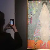 Besucherin fotografiert das größte Gemälde der Welt, ein detailreiches Porträt einer Frau in einem opulenten Kleid, umgeben von bunten Figuren.