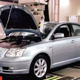 Srebrna Toyota Avensis 2.0 D4D z otwartą maską stoi na stanowisku diagnostycznym.