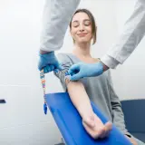 Pobieranie krwi do badań, np. kreatynina czy na czczo. Pacjentka uśmiecha się, gdy pielęgniarka przygotowuje wkłucie.