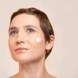 Visage d'une femme avec une touche de crème sur la joue, évoquant la protection contre le soleil pendant une hormonothérapie.