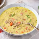 Gęsta zupa z pora z serkiem topionym i mięsem mielonym, ozdobiona koperkiem. Obok talerz z kromkami chleba.
