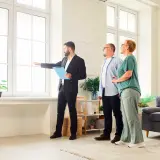 Agente inmobiliario explica a pareja cuánto dura una tasación, señalando la luz natural de la vivienda.