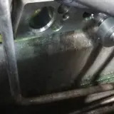 Metalowy blok z otworami, gdzie jest zawór rozprężny klimatyzacji. Widać zielony płyn i rury.