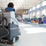 Operator na maszynie czyszczącej dba o sprzątanie hal produkcyjnych.