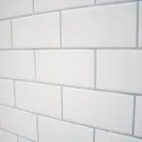 Ściana z białych, prostokątnych płytek z szarymi fugami. Idealna fuga do białych płytek podkreśla ich czystość.