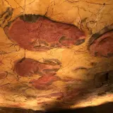 Pinturas rupestres de bisontes en el techo de una cueva, evocando el **museo mitológico Santillana del Mar**.