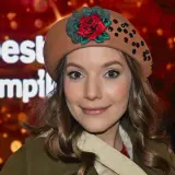 Uśmiechnięta sanah w beretce z różą i błyszczącymi kamieniami, jakby świętowała swoje urodziny.
