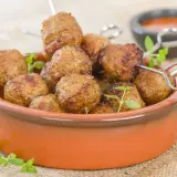 Polpette di tacchino dorate e succulente, cotte nella friggitrice ad aria, servite in una ciotola di terracotta con erbe aromatiche.