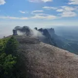 Cumbre rocosa con un monolito en Sant Jeroni, Montserrat. Nubes y montañas se extienden hasta el horizonte.
