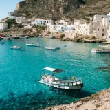 A picturesque harbor with white buildings and boats, showcasing one of the top places to see in Sicily.
