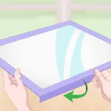 Manos sujetan un marco morado alrededor de una superficie blanca, mostrando cómo hacer una pizarra casera.