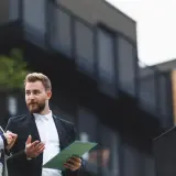 Dwóch agentów nieruchomości dyskutuje, jak wycenić mieszkanie, analizując dokumenty na tle nowoczesnego budynku.