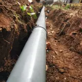 Wykonanie drenażu rozsączającego: szary rów z rurą, przygotowany do odprowadzania wody.