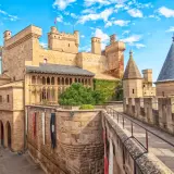 Imponente fortaleza de los castillos de España, con torres cónicas y un patio bajo un cielo azul y nubes blancas.