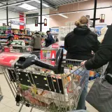 Ludzie robią zakupy w supermarkecie, zastanawiając się, czy w Wielką Sobotę można pracować. Wózek sklepowy pełen produktów.
