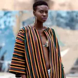 A woman models a vibrant Ankara fabric jacket with bold stripes of red, yellow, green, and black.