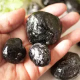 Eine Hand hält mehrere glänzende, schwarze Apachentränen-Steine. Sie sehen aus wie kleine, dunkle Tropfen.