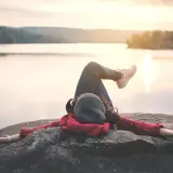Kobieta odpoczywa na skale nad jeziorem, ciesząc się spokojem. To idealny moment na dodatkowy urlop i relaks.