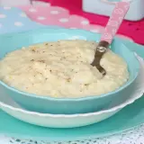 Un cremoso riso e latte, cosparso di cannella, servito in una ciotola azzurra con un cucchiaino rosa.