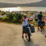 Ciclistas con alforjas exploran **rutas bicicleta** con vistas a un pueblo costero y el mar al atardecer.