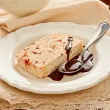 Delizioso semifreddo alla mandorla con salsa al cioccolato su un piatto bianco, pronto per essere gustato.