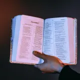 Otwarta księga z tekstem, dłoń przytrzymująca strony. Czy testament bez notariusza jest ważny? Warto szukać odpowiedzi w mądrych księgach.