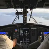 Widok z kokpitu samolotu na wyspy. Piloci w słuchawkach sterują maszyną. Ciekawe, ile zarabia pilot samolotu za taką pracę.