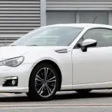 Białe Toyota BRZ z czarnymi felgami stoi przed budynkiem z poziomymi żaluzjami.
