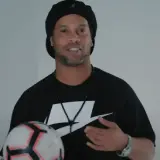Ronaldinho, żyje i trzyma piłkę. Uśmiecha się, ubrany w czarną koszulkę z logo Nike.