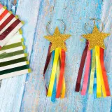Aretes de carnaval manualidades con estrellas doradas y cintas de colores. Un conjunto de cintas de raso de varios tonos a la izquierda.