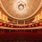 Wnętrze teatru z czerwonymi fotelami i bogato zdobionym sufitem. Czekamy na wspaniały występ.