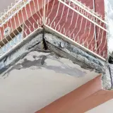 Zniszczony balkon z widocznymi ubytkami w betonie i zardzewiałym zbrojeniem. Idealne miejsce, by zastanowić się, czym uzupełnić ubytki w betonie na zewnątrz.