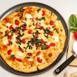 Pyszna pizza z serka wiejskiego, pomidorkami koktajlowymi i bazylią. Obok leżą świeże pomidory i nóż do pizzy.