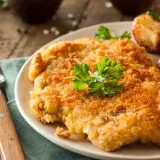 Chrupiący kotlet w złocistej panierce do mięsa, podany z pieczonymi ziemniaczkami i cytryną.