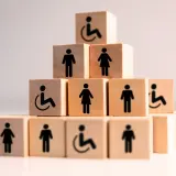 Drewniane klocki tworzą piramidę z symbolami osób, w tym wózka inwalidzkiego, symbolizującymi umiarkowany stopień niepełnosprawności i równość.