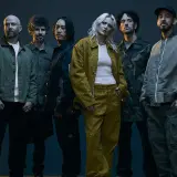 Sześcioro muzyków, w tym wokalistka w żółtym komplecie, pozuje do zdjęcia. Ich styl nawiązuje do **nu metal**owych klimatów.