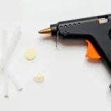 Pistolet do kleju na gorąco, kilka pałeczek kleju, muszelka i żółty krążek. Czy klej na gorąco przewodzi prąd?
