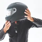 Persona indossa un casco nero, mostrando le sue parti. Le mani regolano il cinturino e la visiera.