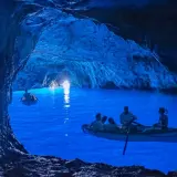Barche a remi navigano nelle magiche grotte blu, illuminate da una luce surreale che rende l'acqua di un blu intenso.