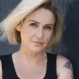 Małgorzata Ohme z blond włosami i tatuażem na ramieniu, na ciemnym tle.