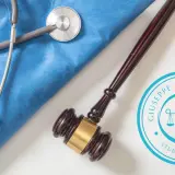 Martelletto da giudice e stetoscopio su camice blu, simboli di giustizia e cura. Studio legale specializzato in casi di malpractice.