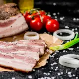Idealny boczek do carbonary: plastry wędzonego boczku, pomidorki, cebula i szczypiorek na czarnym tle.