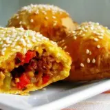 Złociste empanadas posypane sezamem, z widocznym farszem z warzyw i mięsa. Pyszna przekąska.