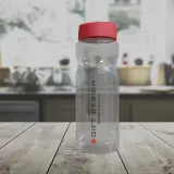 Przezroczysta butelka z czerwonym wieczkiem na drewnianym blacie. Dowiedz się, jak usunąć zapach z plastikowej butelki, aby cieszyć się świeżością.