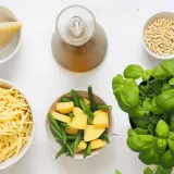 Ingredienti per un pesto senza pinoli: basilico fresco, formaggio grattugiato, patate, fagiolini, olio e aglio.