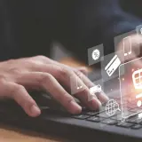 Dłoń na klawiaturze laptopa, nad nią ikony symbolizujące zakupy online: koszyk, karty płatnicze, dostawa. Sukces każdego ecommerce retailer.