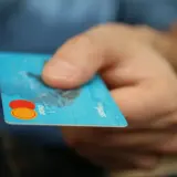 Main tenant une carte bancaire bleue, prêt à effectuer un achat. Il est possible de bloquer un paiement CB en cas de perte.