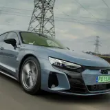 Szary Audi e-tron GT pędzi po drodze, otoczony liniami energetycznymi i słupami wysokiego napięcia.