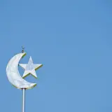 En glänsande halvmåne med en stjärna, en symbol för islam, mot en klarblå himmel.