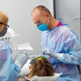 Znieczulenie u dentysty w ciąży. Dwoje stomatologów w fartuchach i maskach wykonuje zabieg u pacjentki.